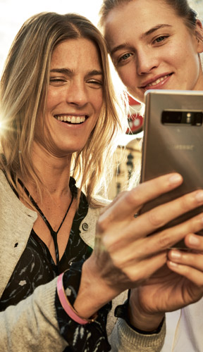 Zwei Frauen schauen lächelnd auf ein Smartphone.