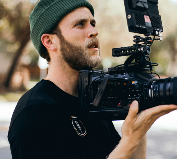 Ein junger Mann mit Vollbart und hipper Mütze hält konzentriert eine professionelle Kamera in der Hand.