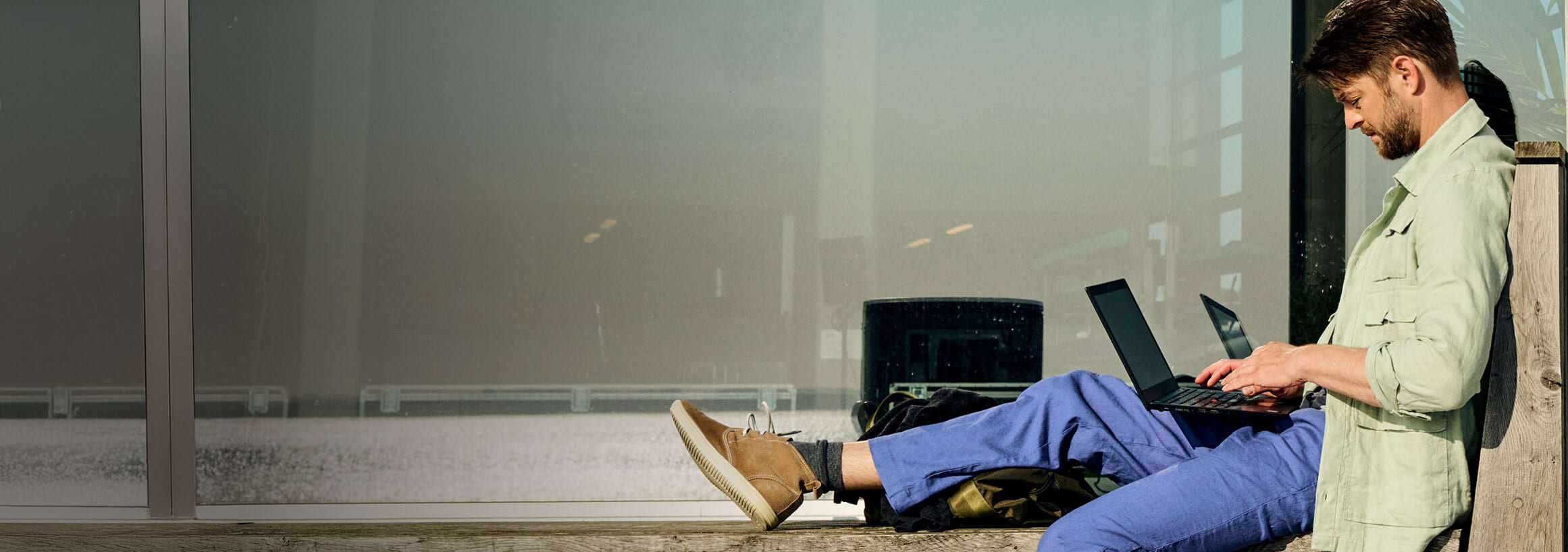 Ein Mann sitzt draußen auf einer Stufe an seinem Laptop und arbeitet.