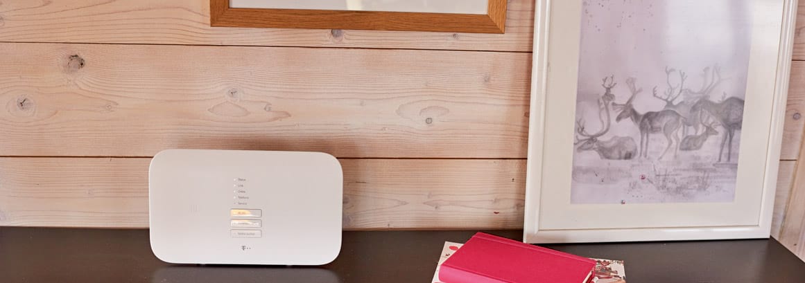 Ein Telekom-Router steht auf einer Anrichte. Um ihn herum ist viel Platz und es liegt lediglich ein Buch auf der Anrichte und ein Bilderrahmen, der gegen die Wand gelehnt ist.