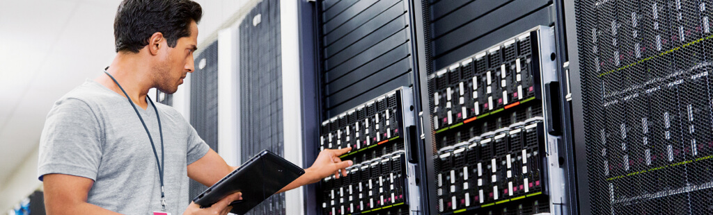 Mann steht im Gnag eines modernen Rechenzentrums und interagiert mit einem der Server.